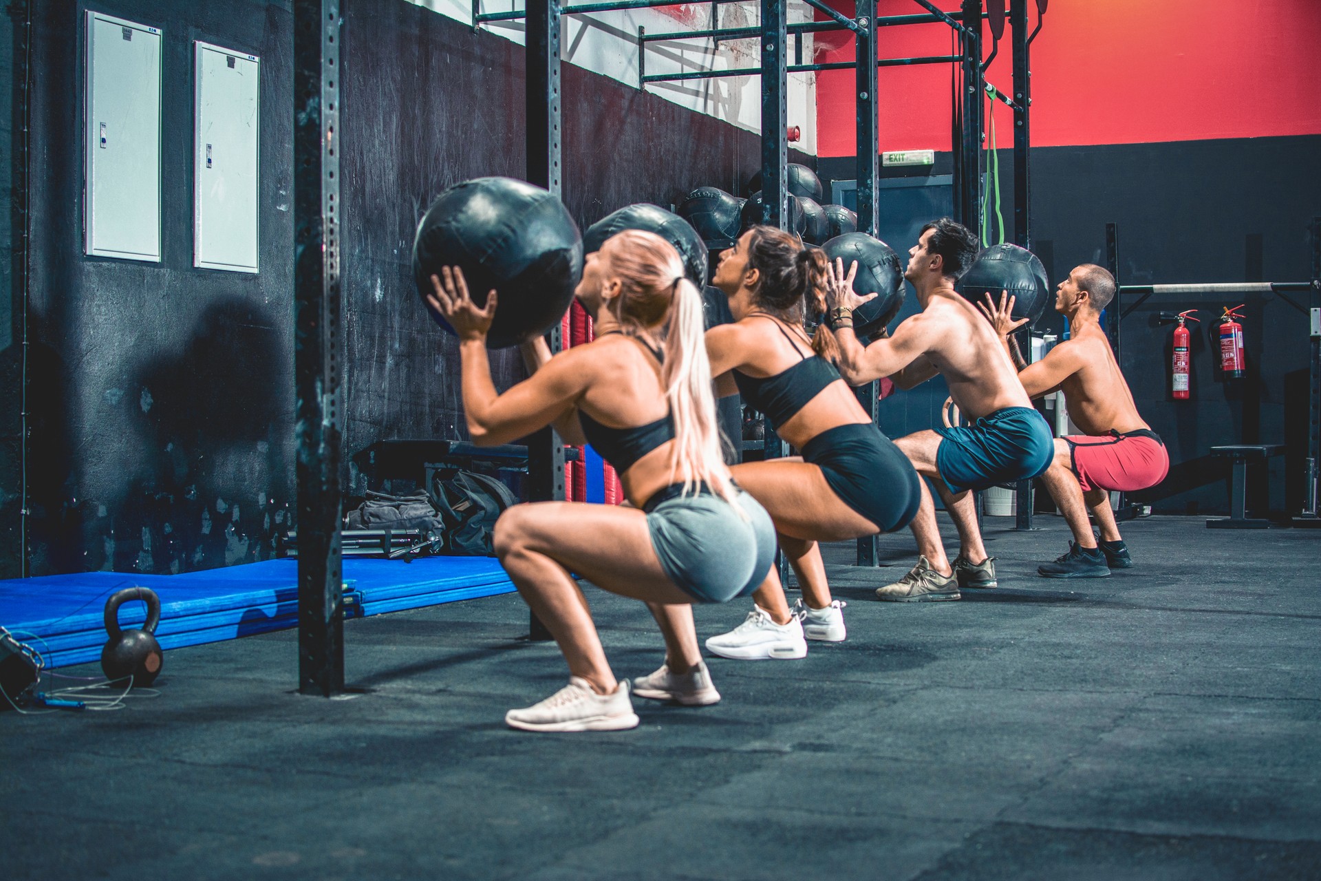 Group of sporty people doing squats with fitness ball in the gym.